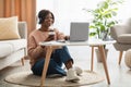 African female using laptop computer drinking coffee sitting at home Royalty Free Stock Photo