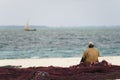 African fisherman sitting on fishing nets looks out to sea