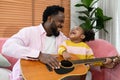 African girl and father are playing guitar while sitting on the sofa at home Royalty Free Stock Photo