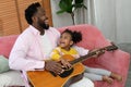 African girl and father are playing guitar and smiling while sitting on couch Royalty Free Stock Photo