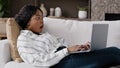 African girl freelancer american biracial woman lying on couch at home looking in laptop reading unexpected bad news Royalty Free Stock Photo