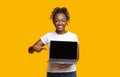 African girl pointing at blank laptop screen over yellow background Royalty Free Stock Photo