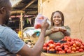 african girl selling tomatoes in a local african market to a male customer smiling while receiving payment