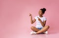 African girl sitting with crossed legs and pointing fingers aside Royalty Free Stock Photo