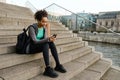 African girl using mobile phone while sitting with yoga mat on stairs outdoors Royalty Free Stock Photo