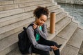 African girl using mobile phone while sitting with yoga mat on stairs Royalty Free Stock Photo