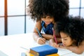 African girls as older and younger sister write or draw something on white paper near the book in front of glass windows with day