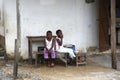 African girls sit in front of a house