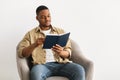 African Guy Reading Book Sitting In Chair Over Gray Background Royalty Free Stock Photo