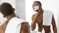 African Guy Shaving Face Covered With Shave Foam In Bathroom