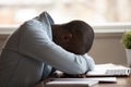 African guy sleeps on hands at table near computer