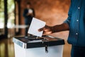 african hand casting a vote paper election ballot in a voting box, brick walls background. african american man putting a