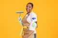 African housekeeper woman holding spray and squeegee over yellow background Royalty Free Stock Photo