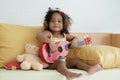 African little cute girl in ear warmers playing ukulele on sofa at home. Christmas concept Royalty Free Stock Photo