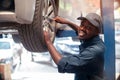 African maintenance male checking tire service via insurance system at garage with smile