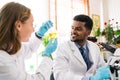 African male scientist researcher evaluates conical flask from Caucasian female assistant to analyze liquid in the lab.