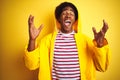 African man with afro hair wearing rain coat with hood standing over isolated yellow background celebrating mad and crazy for