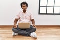 African man with curly hair using laptop sitting on the floor making fish face with lips, crazy and comical gesture