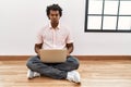 African man with curly hair using laptop sitting on the floor puffing cheeks with funny face Royalty Free Stock Photo