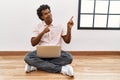 African man with curly hair using laptop sitting on the floor smiling and looking at the camera pointing with two hands and Royalty Free Stock Photo