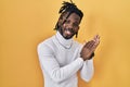 African man with dreadlocks wearing turtleneck sweater over yellow background clapping and applauding happy and joyful, smiling Royalty Free Stock Photo