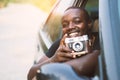 African man driver holding a film camera and smiling while sitting in a car with open front window Royalty Free Stock Photo