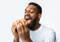 African Man Eating Burger Greedily Enjoying Fastfood Over White Background