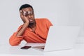 African man with glasses sleeps leaning on his arm sitting at his desk in front of a laptop on a light background