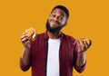 African Man Holding Burger And Slice Of Pizza, Yellow Background