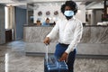 African man hotel guest with suitcase wearing protective mask to protect from coronavirus