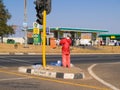 African man in red standing in middle of road waiting for cars to stop to try and sell newspaper to earn a meagre living