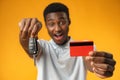 African man showing car key and credit card over yellow background Royalty Free Stock Photo