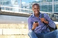 African man sitting outdoors with mobile phone and smiling Royalty Free Stock Photo