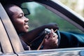 African man traveler holding a film camera and smiling while sitting in a car with open window Royalty Free Stock Photo