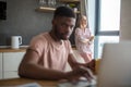 African man using laptop while caucasian girlfriend standing lonely at kitchen Royalty Free Stock Photo