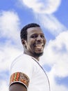 African man wearing a colored Ghanaian tee-shirt and laughing, blue sky, white clouds, photo