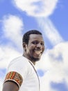 African man wearing a colored Ghanaian tee-shirt and laughing, blue sky, white clouds, photo,