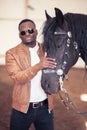 African Man wearing sunglasses near black horse in hangar Royalty Free Stock Photo