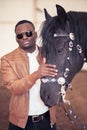 African Man wearing sunglasses near black horse in hangar Royalty Free Stock Photo