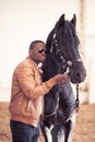 African Man wearing sunglasses near black horse in hangar Royalty Free Stock Photo