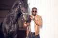 African Man wearing sunglasses near black horse in hangar Royalty Free Stock Photo