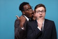 African man whisperingto his caucasian coworker ear telling him secret. Royalty Free Stock Photo