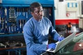 African mechanic man using a laptop computer checking car in workshop Royalty Free Stock Photo