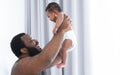 African middle aged bearded father smiling, carrying and soothing newborn baby crying in his arms and hands in bedroom at home.