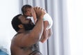 African middle aged bearded father smiling, carrying and soothing newborn baby crying in his arms and hands in bedroom at home.