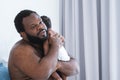 African middle aged bearded father is soothing newborn baby crying in his arms and shoulder in bedroom at home. Single dad hugging Royalty Free Stock Photo