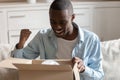 African guy looking inside carton box pleased with received parcel Royalty Free Stock Photo