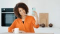 African millennial woman with curly hair girl in orange blouse female vlogger in kitchen at home taking photo on mobile Royalty Free Stock Photo