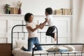 African mom holding hands of little son jumping on bed Royalty Free Stock Photo