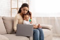 African Mom Working On Laptop Holding Baby Sitting At Home